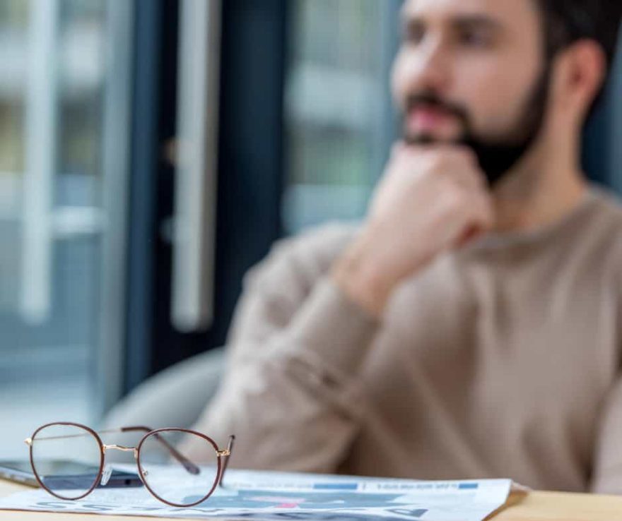 Homme réfléchissant à la transformation digitale avec des documents et lunettes sur la table.