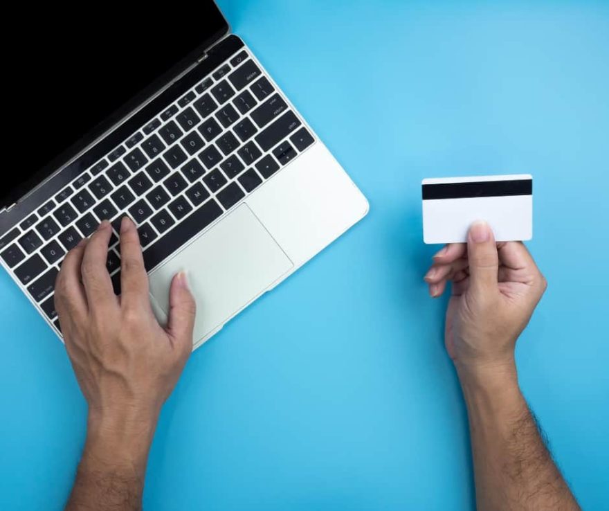 Personne tenant une carte bancaire à côté d’un ordinateur portable.