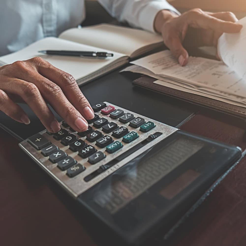 Personne utilisant une calculatrice avec des documents et un stylo.