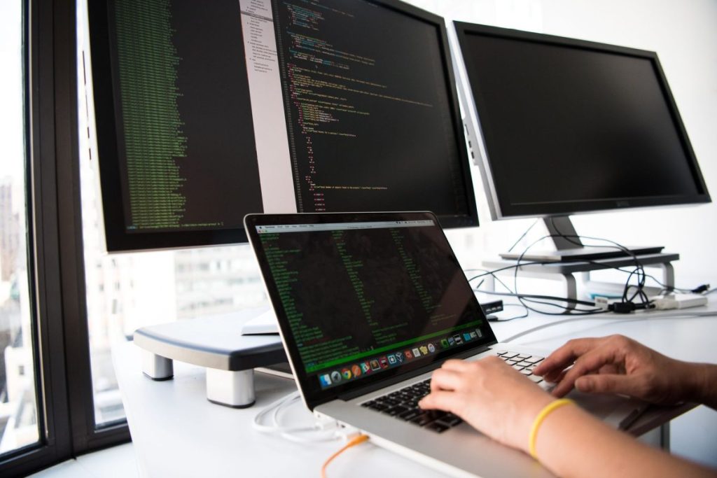 Développeuse travaillant sur un ordinateur portable devant deux écrans : maintenance et sécurité d’un site WordPress