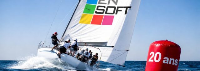 Voilier de course avec équipage naviguant près d'une bouée rouge "20 ans".