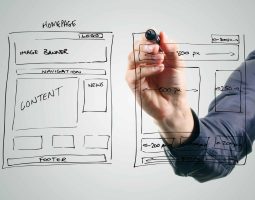 Personne dessinant une maquette de site internet sur tableau blanc.